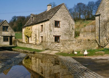 Bahar güneşinde eski nehrin kıyısındaki Cotswold taştan kulübeleri, Duntisbourne Leer, Cotswolds, Gloucestershire, İngiltere