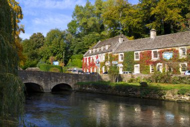 Bibury, Gloucestershire, İngiltere - 7 Ekim 2010: Bibury 'deki River Coln üzerindeki eski köprünün klasik sonbahar manzarası. Bibury bir zamanlar William Morris (1834-96) tarafından 