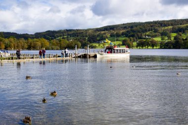 Coniston, İngiltere - 14 Eylül 2011: Cumbria, İngiltere 'de bulunan Lake District Ulusal Parkı' ndaki Coniston Water üzerinde Coniston köyü yakınlarındaki bir rıhtımdan yolcu almak için sonbahar güneşinin erken saatlerinde bir gezi teknesi bekliyor. Coniston Suyu 'dur.
