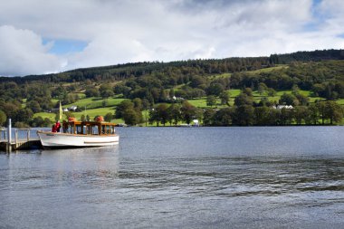 Coniston, İngiltere - 14 Eylül 2011: Cumbria, İngiltere 'de bulunan Lake District Ulusal Parkı' ndaki Coniston Water üzerinde Coniston köyü yakınlarındaki bir rıhtımdan yolcu almak için sonbahar güneşinin erken saatlerinde bir gezi teknesi bekliyor. Coniston Suyu 'dur.
