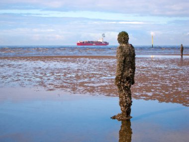 Crosby Beach, İngiltere - 18 Eylül 2011: 100 dökme demirden heykelden biri, bir konteynır gemisinin denizden geçişini seyrediyor. Bir başka yer ise Antony Gormley 'in 100 dökme demir figürden oluşan modern bir heykel enstitüsü. 