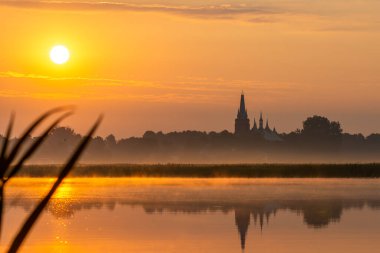 Popowo ve Bug nehri üzerinde sisli bir güneş doğuyor.