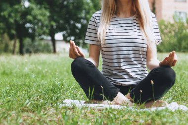 Kız çimlerin üzerinde meditasyon yapıyor. Bir kız sabahın erken saatlerinde yoga matında meditasyon yapıyor. Yeşil bahçede pilates ve fitness. Sabah jimnastiği
