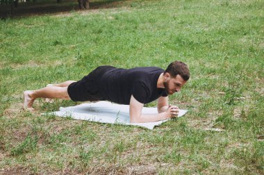 Genç bir adam yeşil bir tropikal bahçeyle çevrili yoga yaparken doğa, esneme, meditasyon ve sağlıkta dinleniyor. Muay Thai gibi çarpıcı teknikler, açık havada karate