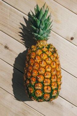 Sarı-beyaz arka planda olgun sulu tropikal ananas. Mesaj için yer var. Tahta bir masada ananas.