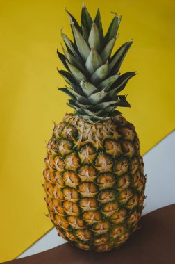 Sarı-beyaz arka planda olgun sulu tropikal ananas. Mesaj için yer var. Tahta bir masada ananas.