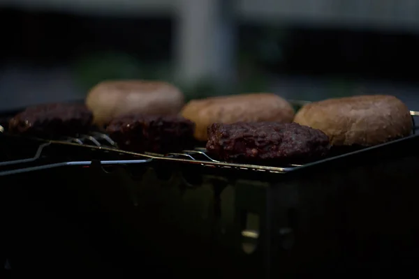 Carne suculenta, frita num grelhador com pão para o hambúrguer. Jantar à noite na fogueira — Fotografia de Stock