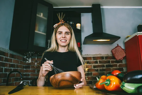 a happy young woman cooks healthy vegetarian food in a loft style kitchen and looks at the recipe on her laptop