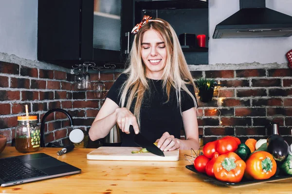 a happy young woman cooks healthy vegetarian food in a loft style kitchen and looks at the recipe on her laptop