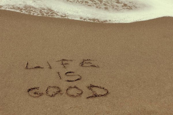 "Надпись "Жизнь хороша" написана на песчаном пляже и приближается волна