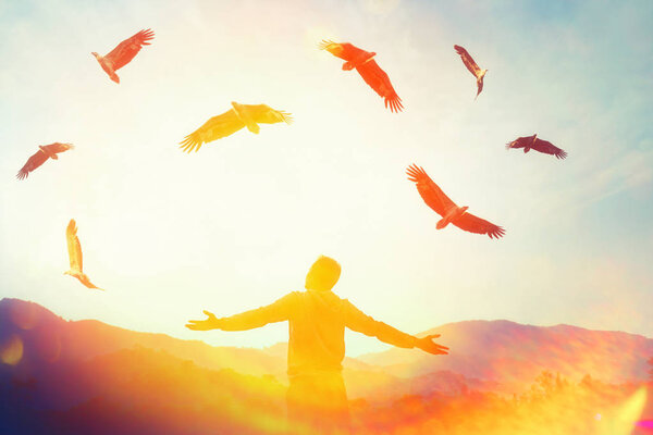 Man raise hand up on top of mountain and sunset sky with eagle birds fly abstract background. Copy space freedom travel adventure and business victory concept. Vintage tone filter effect color style.