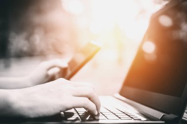 Kadın eli açık doğa parkı ve günbatımı gökyüzü bokeh ışık arka plan ile akıllı telefon ve dizüstü bilgisayar kullanarak. Teknoloji iş ve serbest çalışma kavramı. Vintage sesi filtre efekti renk stili.