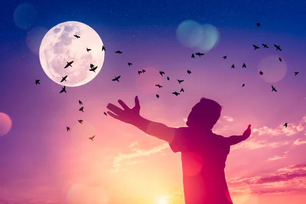 Copy space man raise hand up on sunset sky and birds fly with full moon abstract background. Freedom travel adventure and business victory concept. Vintage tone filter effect color style.
