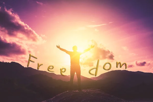 Freedom words on man rise hand up on top of mountain and sunset sky abstract background. Freedom and travel adventure concept. Vintage tone filter effect color style.