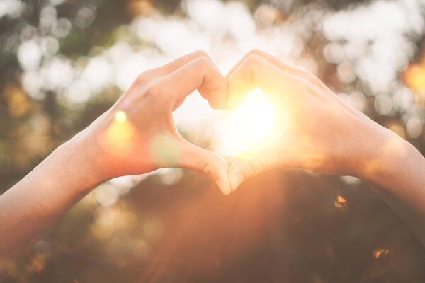 Female hands heart shape on nature bokeh sun light flare and blur leaf abstract background. Copy space of happy love and freedom concept. Vintage tone filter color style.