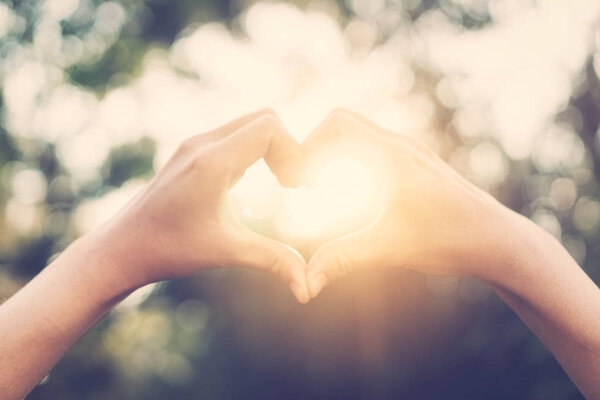 Female hands heart shape on nature bokeh sun light flare and blur leaf abstract background. Copy space of happy love and freedom concept. Vintage tone filter color style.