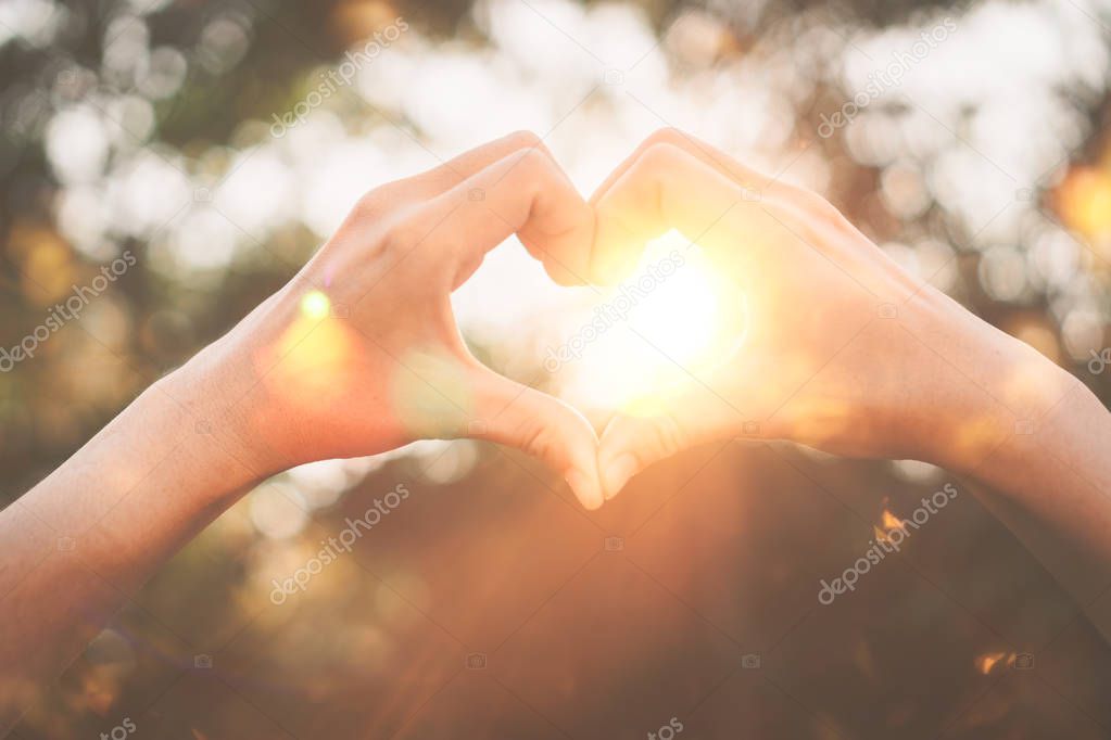 Female hands heart shape on nature bokeh sun light flare and blur leaf abstract background. Copy space of happy love and freedom concept. Vintage tone filter color style.