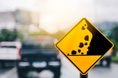 Falling stone warning traffic sign on blur road with colorful bokeh light abstract background. clipart