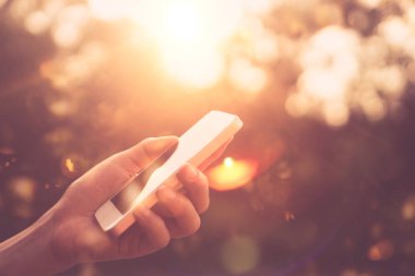 Kadın eli açık doğa Park günbatımı gökyüzü arka plan ile akıllı telefon kullanma.