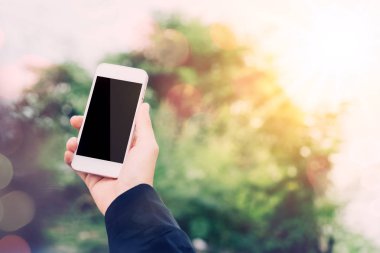 Kadın elini tut akıllı telefon doğa park açık yeşil bokeh ışık arka plan kullanma.