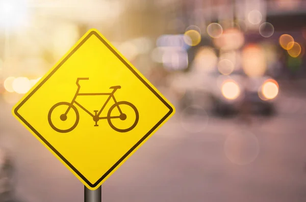 Bicycle warning sign on blur traffic road with colorful bokeh light abstract background. — Stock Photo, Image