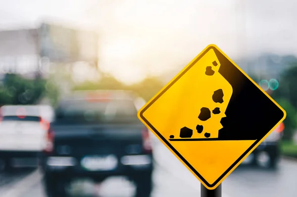 Falling stone warning traffic sign on blur road with colorful bokeh light abstract background. — Stock Photo, Image