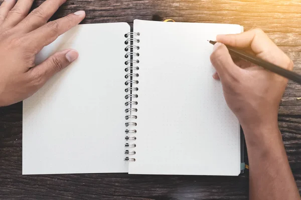 Vista superior de la mano del hombre usando cuaderno sobre fondo de textura de mesa de madera en la cafetería . —  Fotos de Stock