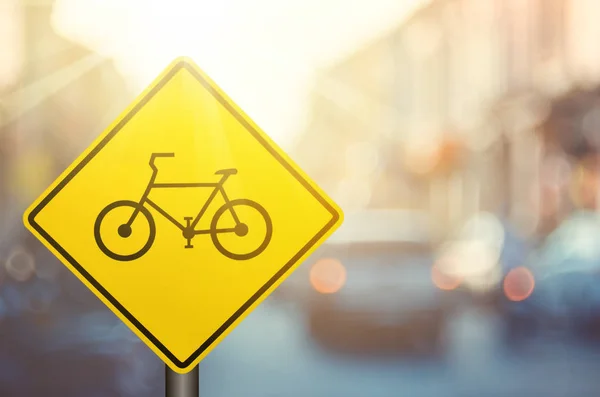 Bicycle warning sign on blur traffic road with colorful bokeh light abstract background. — Stock Photo, Image