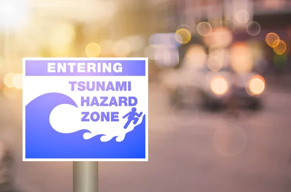 Tsunami hazard zone warning sign on blur traffic road with colorful bokeh light abstract background. — Stock Photo, Image