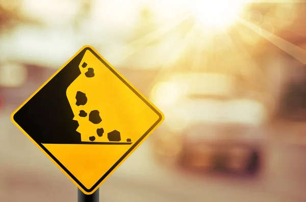 Falling kamień ostrzeżenie znaku drogowego na drodze rozmycie bokeh kolorowe tło światło. — Zdjęcie stockowe