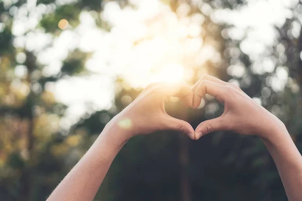 Vrouwelijke handen hart vorm op natuur bokeh zon licht flare en blad abstracte achtergrond wazig. — Stockfoto