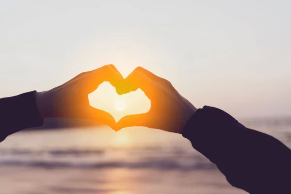 Mujeres manos forma de corazón en la naturaleza bokeh sol luz llamarada ola y borrosa playa tropical fondo abstracto . — Foto de Stock