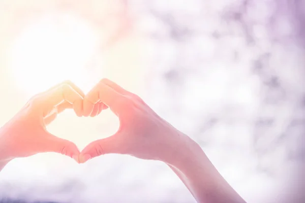 Female hands heart shape on nature bokeh sun light flare and blur leaf abstract background. — Stock Photo, Image