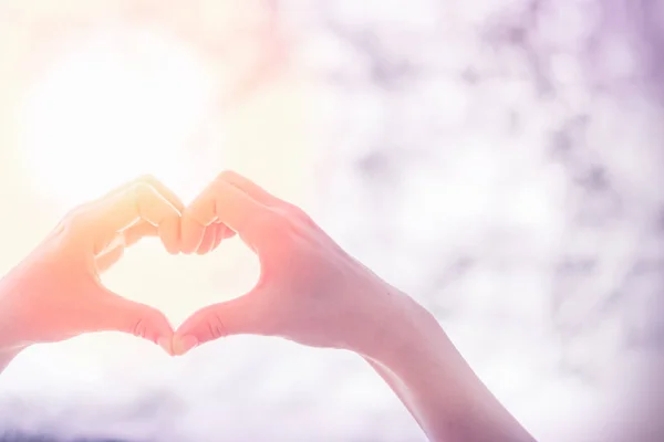 Weibliche Hände Herzform auf Natur Bokeh Sonnenlicht Fackel und verschwimmen Blatt abstrakten Hintergrund. — Stockfoto