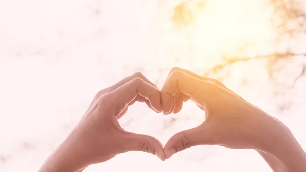 Weibliche Hände Herzform auf Natur Bokeh Sonnenlicht Fackel und verschwimmen Blatt abstrakten Hintergrund. — Stockfoto