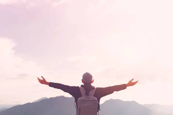 Backpacker Mann heben die Hand oben auf dem Berg mit Sonnenuntergang Himmel und Wolken abstrakten Hintergrund. — Stockfoto