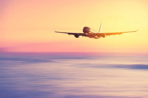 Airplane flying over blur tropical beach with smooth wave and sunset sky abstract background. — Stock Photo, Image