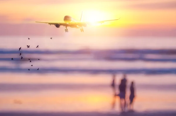 Airplane flying over blur people relax on tropical sunset beach with bokeh sun light wave abstract background.