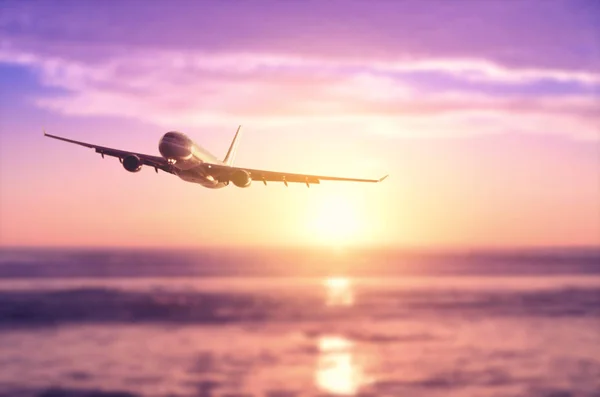 Airplane flying over blur tropical beach with smooth wave and sunset sky abstract background. — Stock Photo, Image