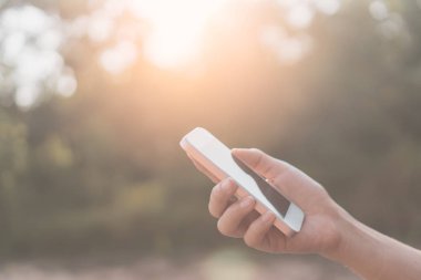 Kadın eli açık doğa Park günbatımı gökyüzü arka plan ile akıllı telefon kullanma.