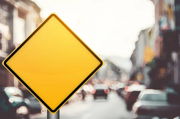 Signo de tráfico amarillo vacío en la carretera de tráfico borroso con colorido fondo abstracto de luz bokeh . — Foto de Stock