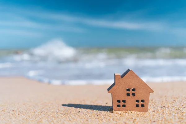 Small home model on sand beach with blue sky background.