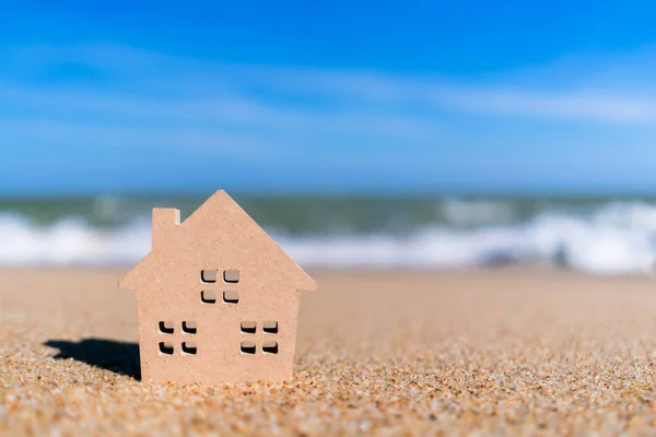 Pequeño modelo de casa en la playa de arena con fondo azul cielo . — Foto de Stock