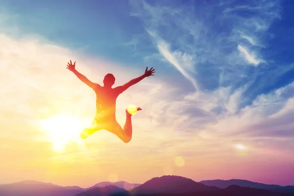 Glücklicher Mann springt auf dem Gipfel des Berges mit Sonnenuntergang Himmel abstrakten Hintergrund. — Stockfoto