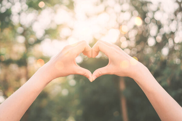 Female hands heart shape on nature bokeh sun light flare and blur leaf abstract background.