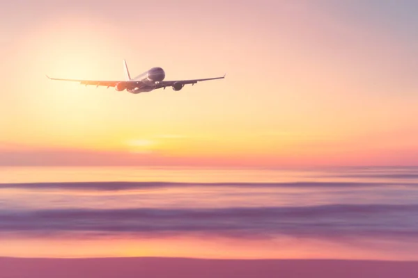 Airplane flying over tropical beach with smooth wave and sunset sky abstract background. — Stock Photo, Image