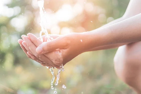stock image Water from tap to woman hand in nature green park sunset time and bokeh sun light abstract background.