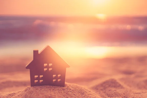 Small home model on sunset beach sand texture background.