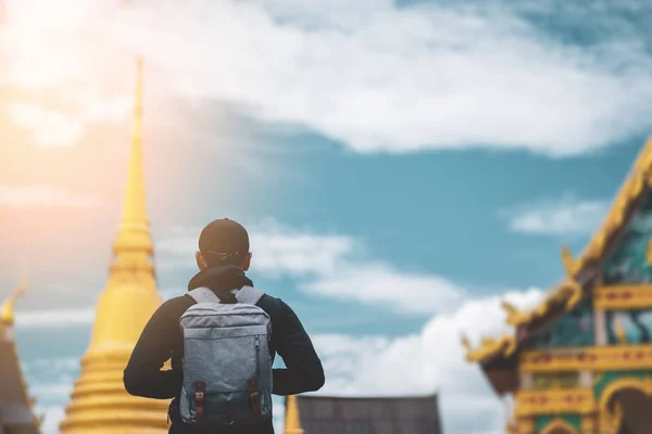 Backpack man standing front of blur temple Thailand with blue sky and white cloud background.