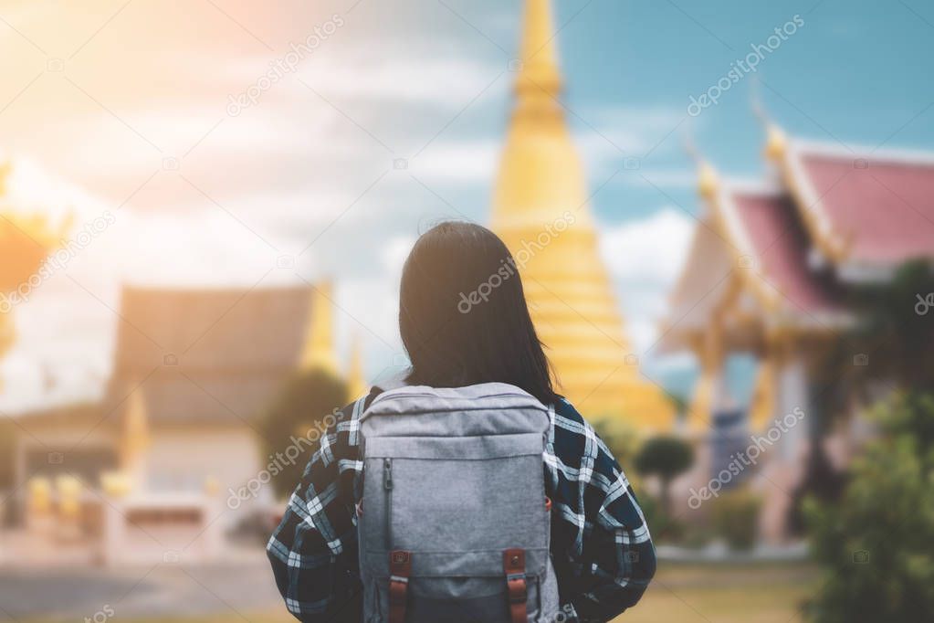 Backpack woman standing front of blur temple Thailand with blue sky and white cloud background.